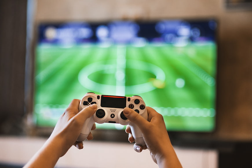 Hands holding white game controller playing soccer video game