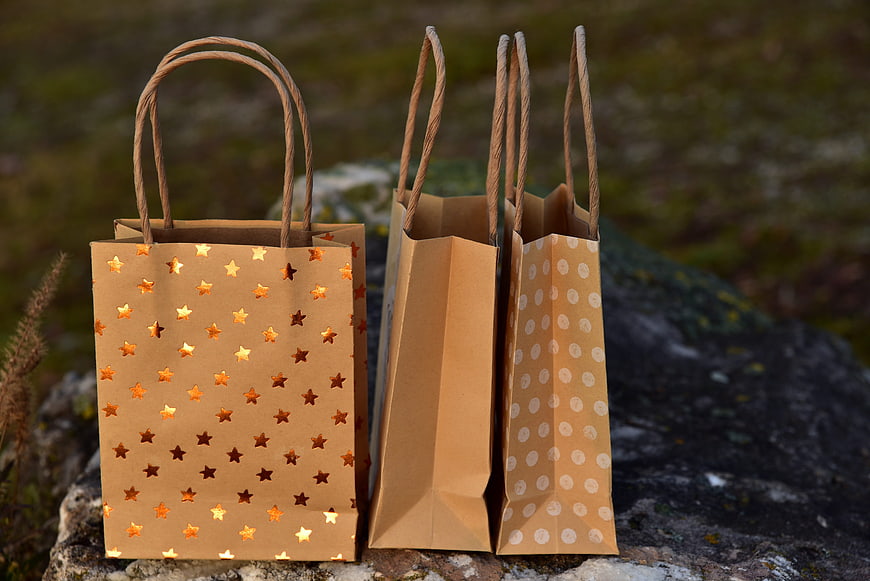 Three decorative kraft paper gift bags with star and dot patterns on a rock