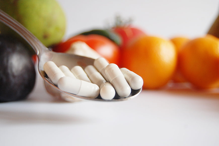 White vitamin capsules on spoon with fresh fruit background