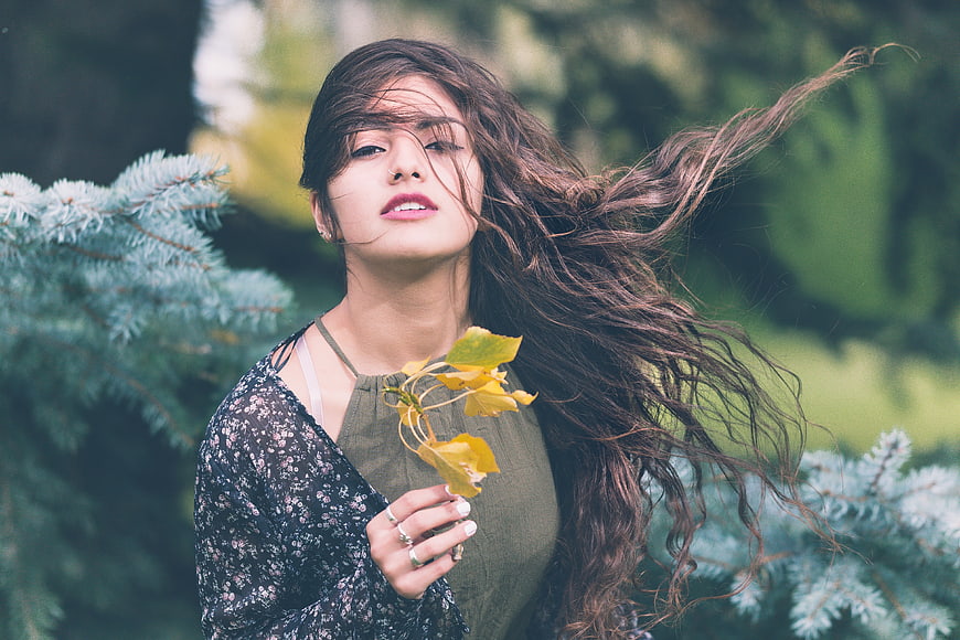 Woman with Windblown Hair Holding Yellow Leaves in Forest