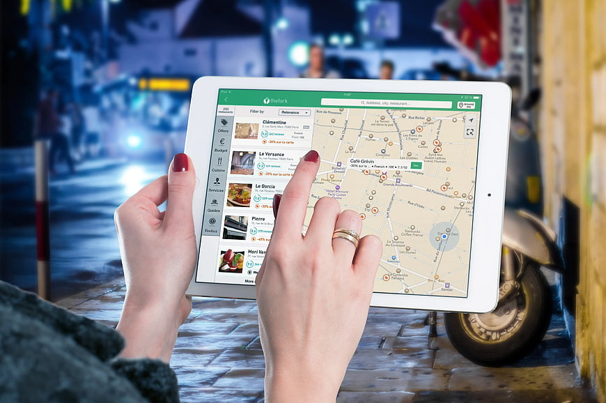 Hands using tablet app to find restaurants on city street at night