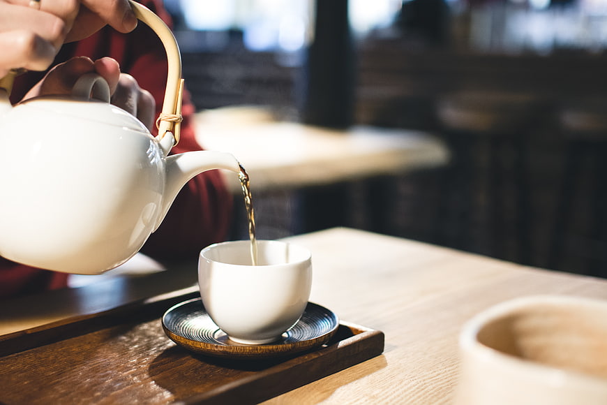Pouring hot tea from white ceramic teapot into cup