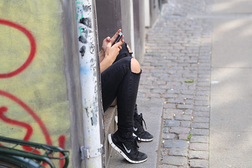Teenage girl texting on smartphone sitting on urban sidewalk