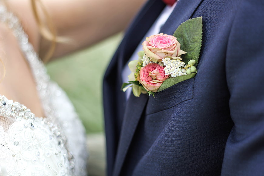 Close-up of groom's boutonniere and bride's dress at wedding