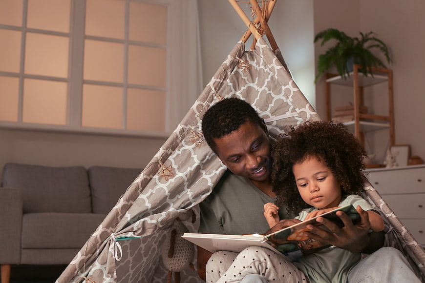 Father and daughter reading together in a cozy indoor tent