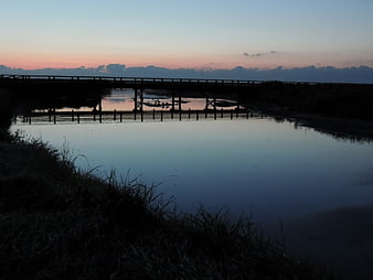 Silhouette of wooden bridge over calm river at sunrise