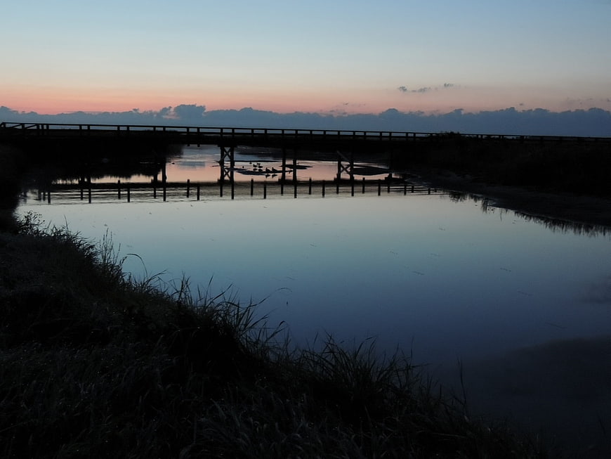 Silhouette of wooden bridge over calm river at sunrise
