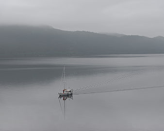 Lone sailboat on calm foggy lake with mountains