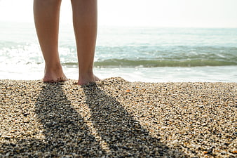 Close-up of bare feet standing on pebbly beach sand