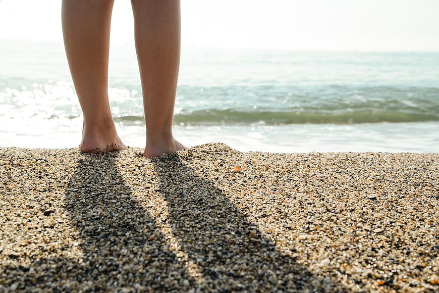 Close-up of bare feet standing on pebbly beach sand