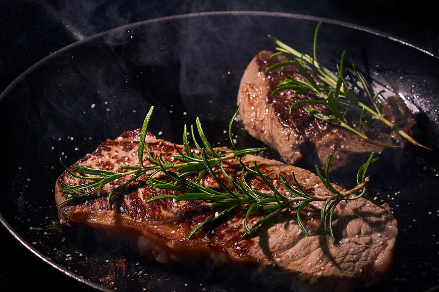 Sizzling Grilled Steak With Fresh Rosemary Sprigs In Cast Iron Pan