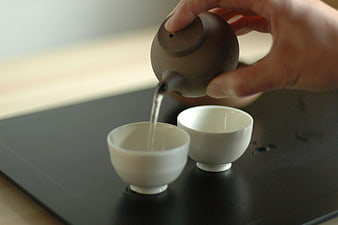 Hand Pouring Tea from Ceramic Teapot into White Cups