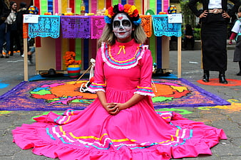 Woman in traditional pink dress and sugar skull makeup at Day of the Dead festival