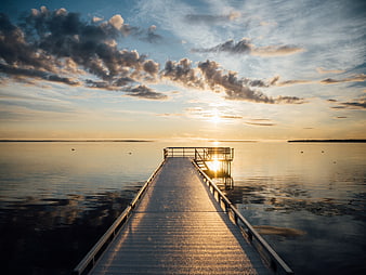 Sunset over a wooden pier on a calm lake with clouds