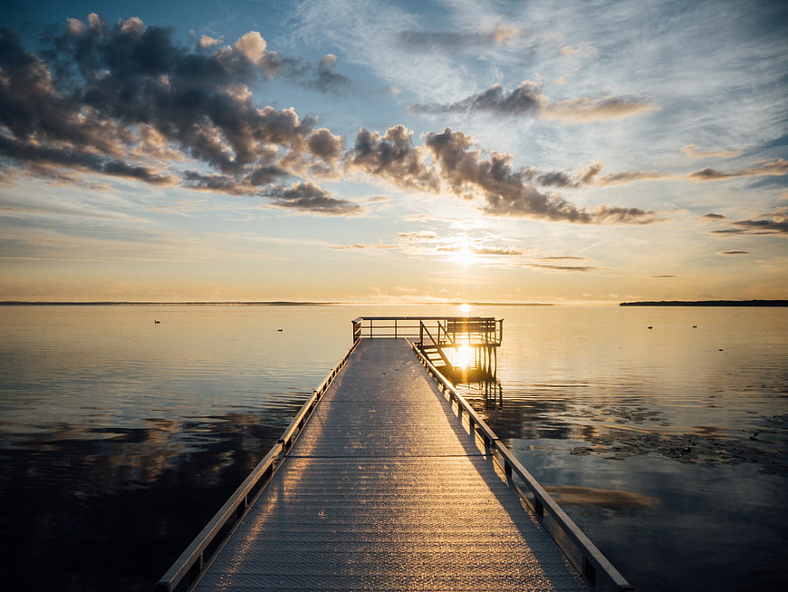Sunset over a wooden pier on a calm lake with clouds
