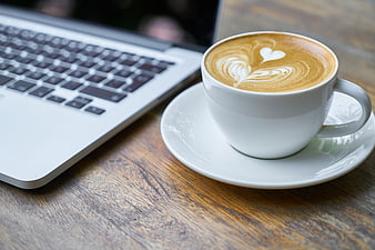 Latte with heart art next to laptop on wooden table