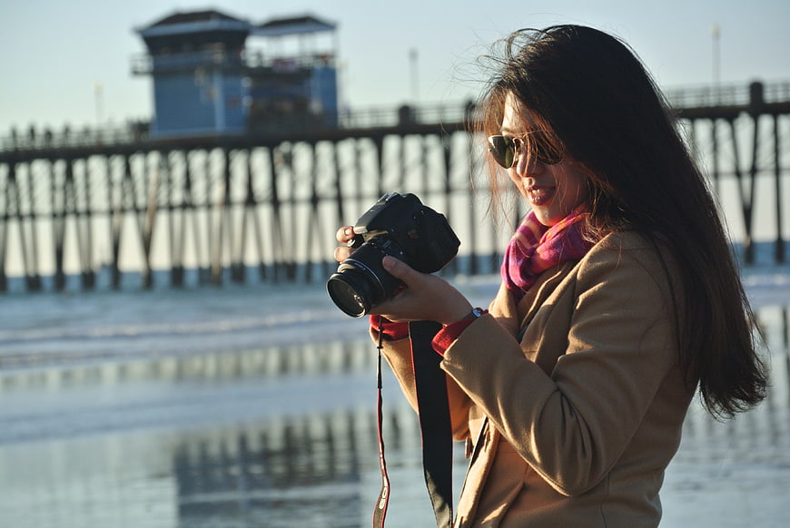 Woman with Camera on Beach with Pier Background