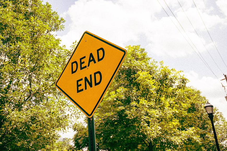 Yellow Dead End Road Sign Against Green Trees and Sky