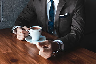 Businessman in Suit Holding White Coffee Cup on Wooden Table