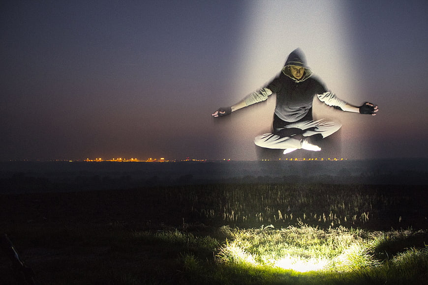 Man Levitating in Meditation Pose Under Spotlight at Night