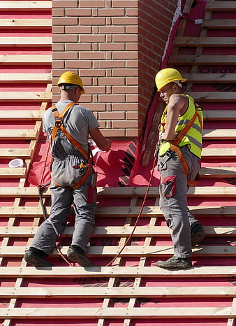 Two construction workers in safety gear on a building roof