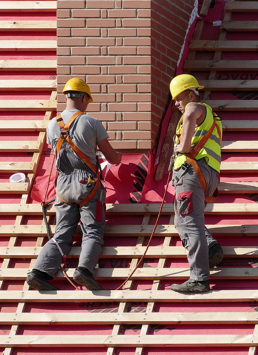 Two construction workers in safety gear on a building roof