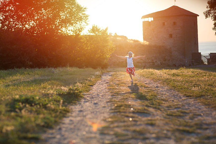 Happy little girl running on path at sunset near tower
