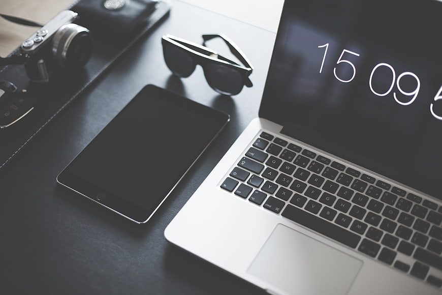 Modern workspace with laptop, tablet, camera, and sunglasses