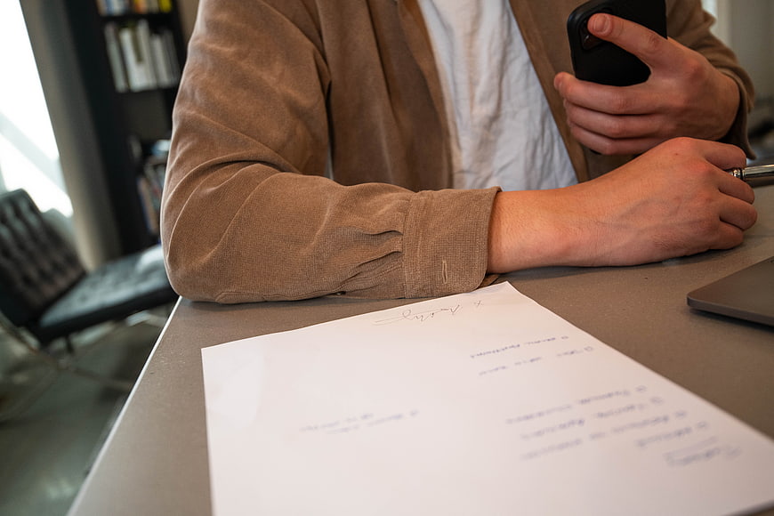 Person signing contract while checking smartphone at desk