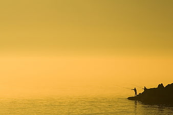 Silhouettes of fishermen on rocky coast in golden fog