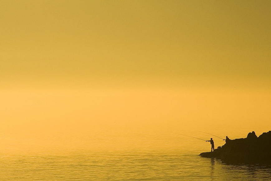 Silhouettes of fishermen on rocky coast in golden fog
