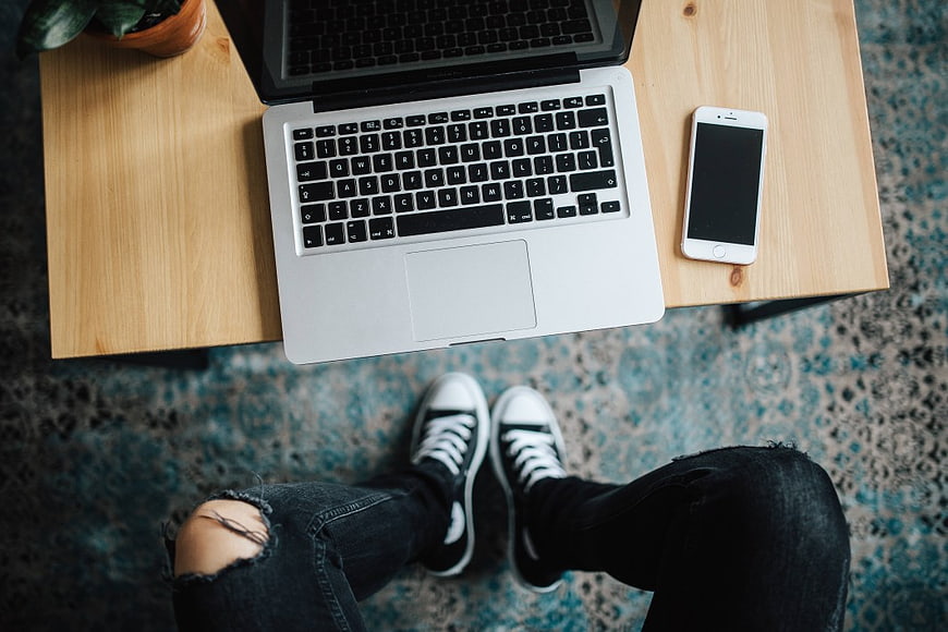 Top-down view of laptop and smartphone on wooden desk with legs