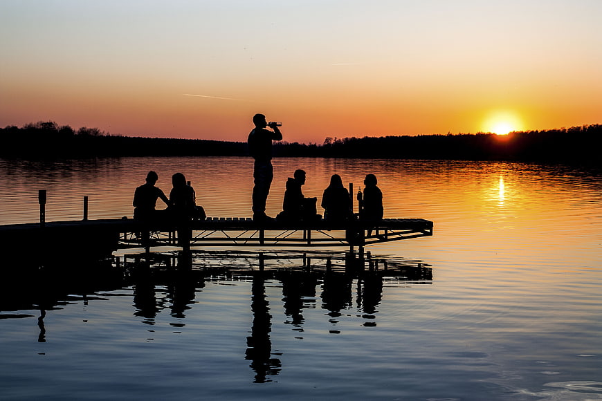 Silhouettes of Friends Relaxing on Dock at Sunset