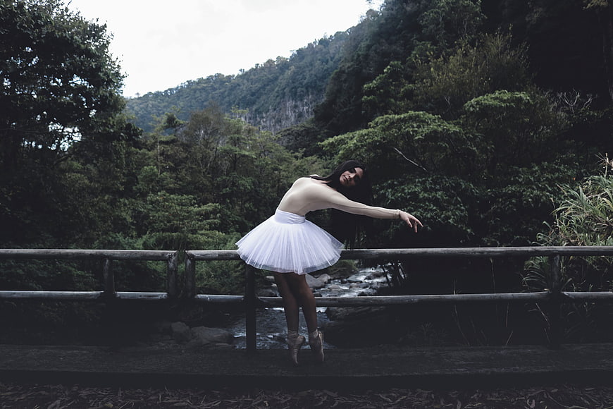 Ballerina in white tutu posing on bridge in forest