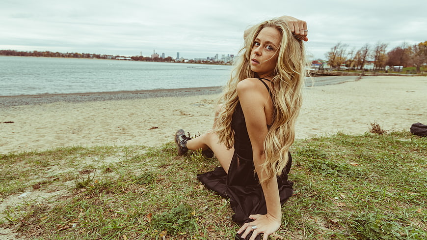 Blonde Woman in Black Dress Sitting on Beach