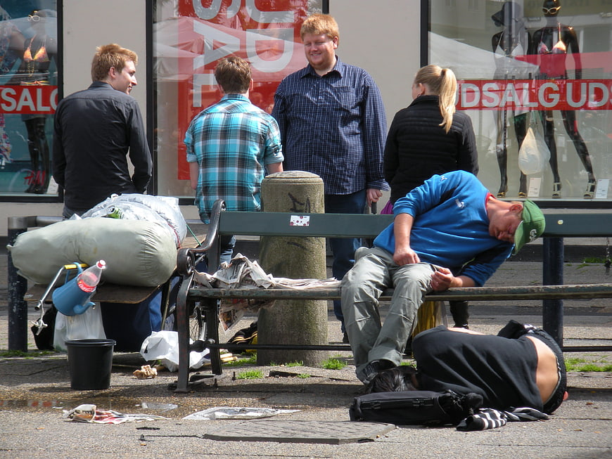 Homeless men sleeping on street bench with passersby