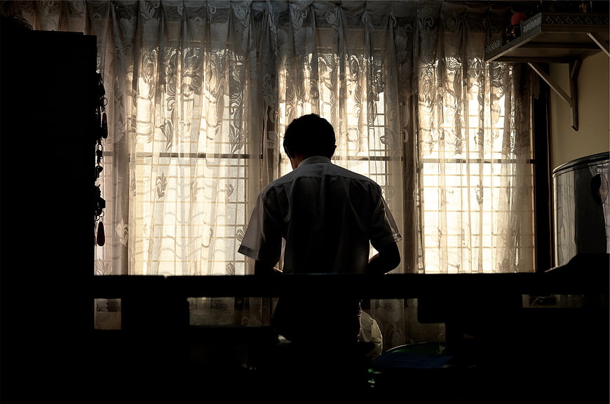 Silhouette of Man Looking Out Window Through Curtains