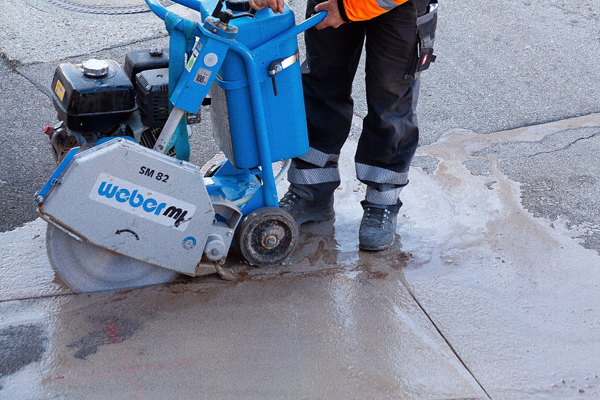 Construction worker operating blue concrete saw on wet pavement