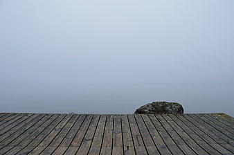 Minimalist wooden dock planks in thick fog with rock