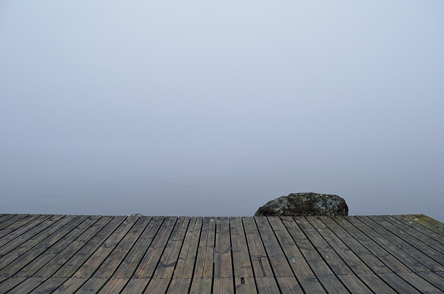 Minimalist wooden dock planks in thick fog with rock