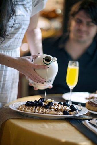 Woman pouring syrup on waffles with berries and orange juice