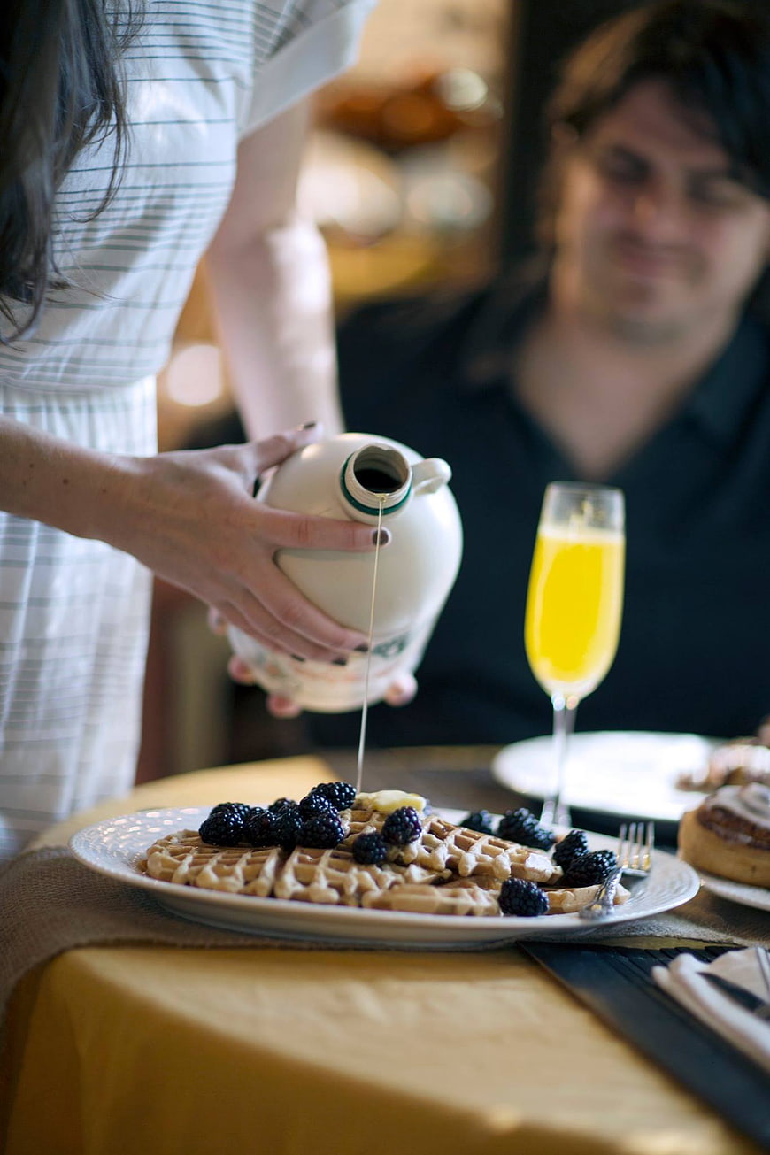 Woman pouring syrup on waffles with berries and orange juice