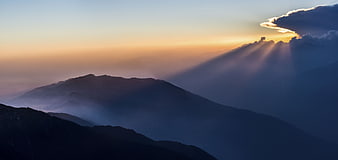 Dramatic sun rays breaking through clouds over misty mountain landscape