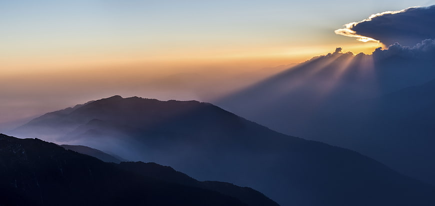 Dramatic sun rays breaking through clouds over misty mountain landscape