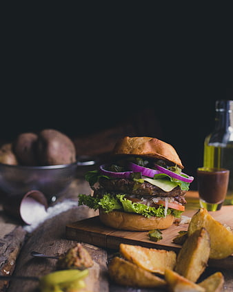 Gourmet burger with potato wedges on rustic wooden board