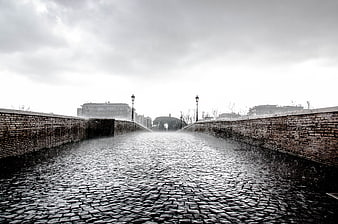 Rainy cobblestone bridge with brick walls and street lamps