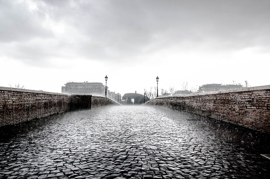 Rainy cobblestone bridge with brick walls and street lamps