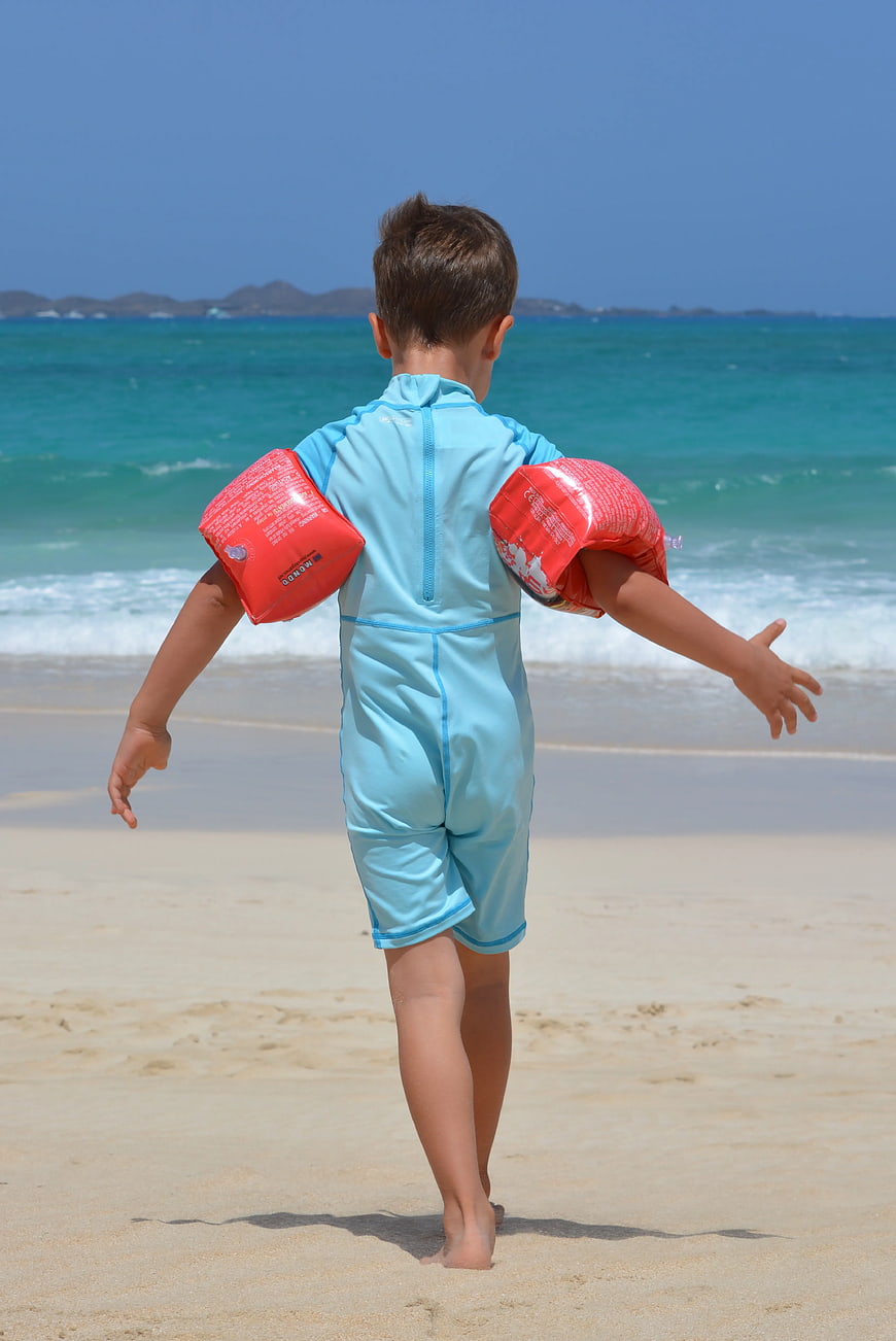 Boy with Red Arm Floats Running Toward Ocean Beach