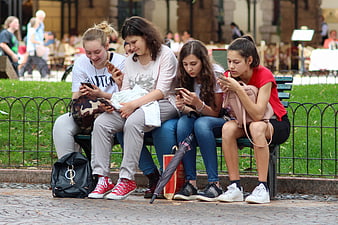 Teenage girls sitting on park bench using smartphones