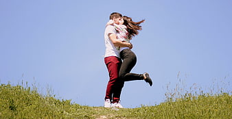 Romantic couple embracing and kissing on a grassy hill under a clear blue sky